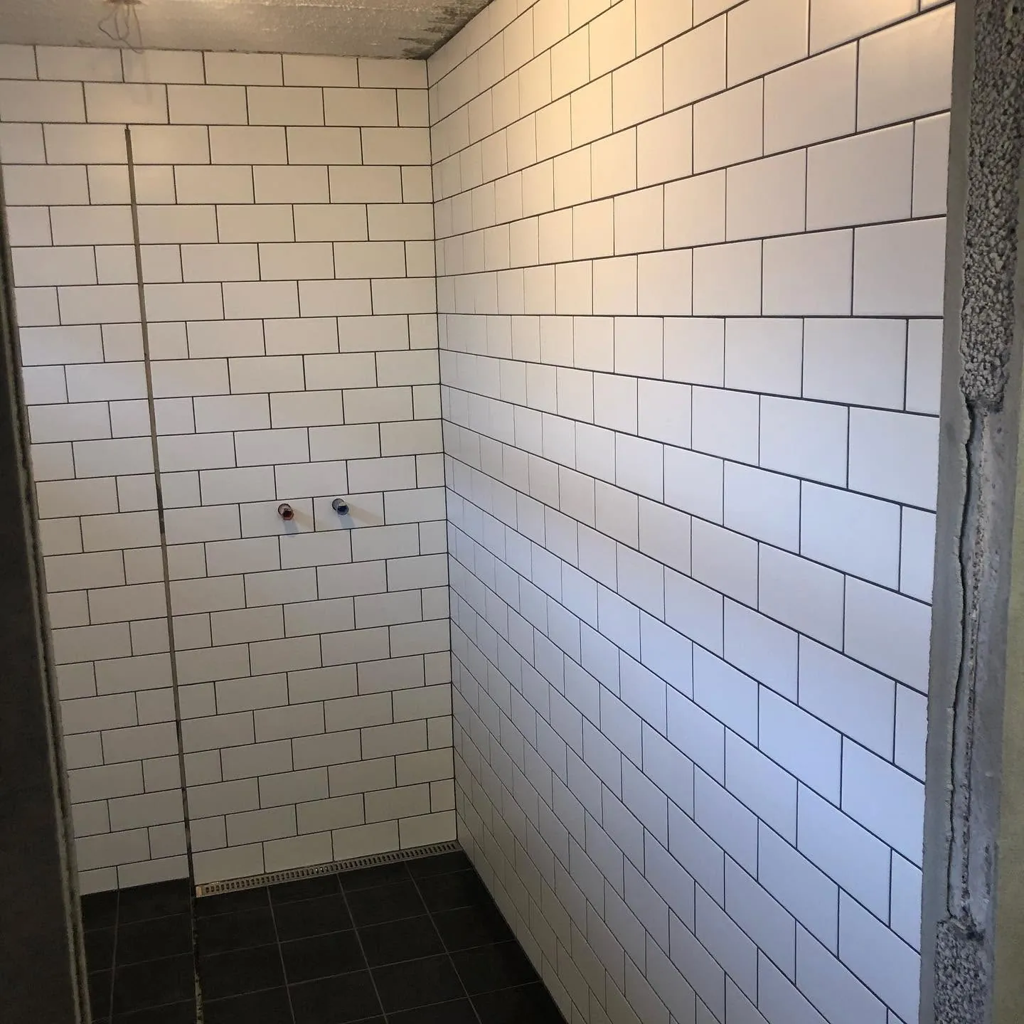 Hvítar subway-flísar á sturtuvegg og svartar gólfflísar
